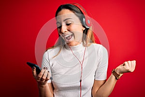 Young beautiful brunette woman listening to music using smartphone and headphones screaming proud and celebrating victory and