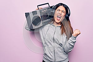 Young beautiful brunette woman listening to music using vintage boombox and headphones screaming proud, celebrating victory and