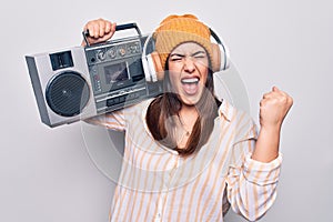 Young beautiful brunette woman listening to music using vintage boombox and headphones screaming proud, celebrating victory and