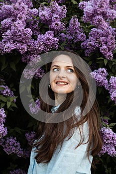 Young beautiful brunette woman is smelling lilac flower blossom in spring time