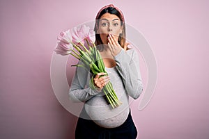 Young beautiful brunette woman pregnant expecting baby holding bouquet of tulips cover mouth with hand shocked with shame for