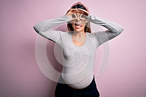 Young beautiful brunette woman pregnant expecting baby over isolated pink background doing ok gesture like binoculars sticking