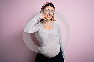 Young beautiful brunette woman pregnant expecting baby over isolated pink background smiling doing phone gesture with hand and