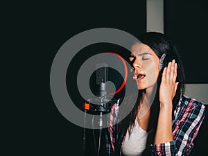 Young beautiful brunette woman recording voice, song or album in professional studio. Girl sings near microphone in