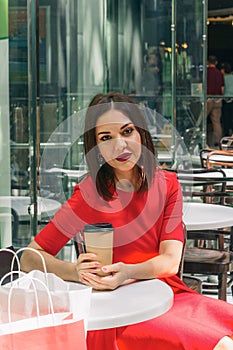 Beautiful brunette woman in red dress drinking coffee in a coffee shop