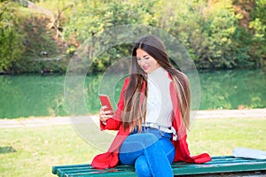 Young beautiful brunette woman with red lips and long straight hair wearing red jacket sitting outdoor in autumn park.