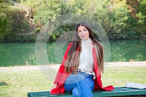 Young beautiful brunette woman with red lips and long straight hair wearing red jacket sitting outdoor in autumn park.