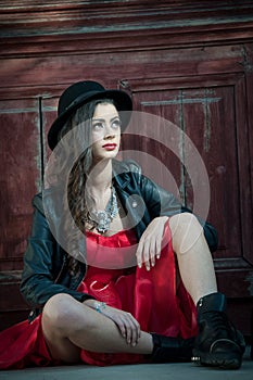 Young beautiful brunette woman with red short dress and black hat posing sensual in vintage scenery. Romantic mysterious lady