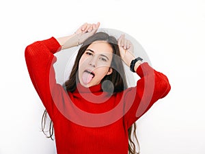 Young beautiful brunette woman in red sweater showing horns with her fingers posing against white background