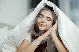 Young beautiful brunette woman sitting in bed with blanket on her head with her hands near her face in the morning