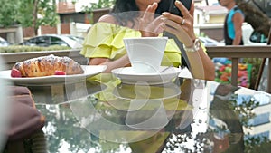 Young beautiful brunette woman sitting in an outdoor cafe, drinking coffee and using a phone