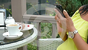 Young beautiful brunette woman sitting in an outdoor cafe, drinking coffee and using a phone