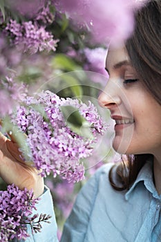 Young beautiful brunette woman is smelling lilac flower blossom in spring time