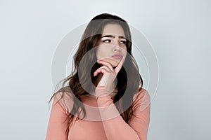 Young beautiful brunette woman standing on isolated white background looking hesitant , pure beauty