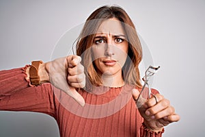 Young beautiful brunette woman using eyelash curler over isolated white background with angry face, negative sign showing dislike