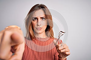 Young beautiful brunette woman using eyelash curler over isolated white background pointing with finger to the camera and to you,