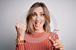 Young beautiful brunette woman using eyelash curler over isolated white background screaming proud and celebrating victory and