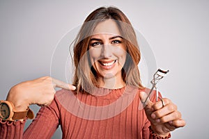 Young beautiful brunette woman using eyelash curler over  white background with surprise face pointing finger to himself