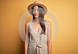 Young beautiful brunette woman on vacation wearing casual dress and hat smiling looking to the side and staring away thinking