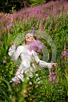 Young beautiful brunette woman walking through wildflowers in alpine meadow, summer dress, mountain, sunlight