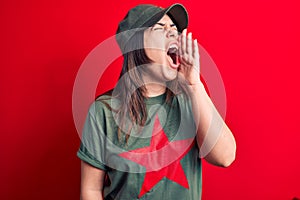 Young beautiful brunette woman wearing cap and t-shirt with red star communist symbol shouting and screaming loud to side with