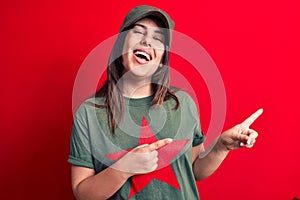 Young beautiful brunette woman wearing cap and t-shirt with red star communist symbol smiling and looking at the camera pointing