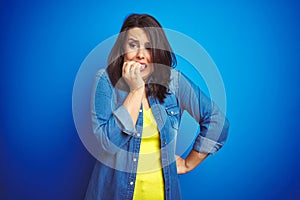 Young beautiful brunette woman wearing casual blue denim jacket over blue isolated background looking stressed and nervous with