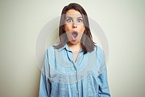 Young beautiful brunette woman wearing casual blue denim shirt over isolated background afraid and shocked with surprise
