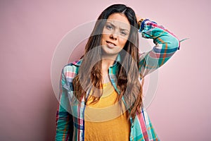 Young beautiful brunette woman wearing casual colorful shirt standing over pink background confuse and wonder about question