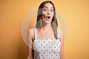 Young beautiful brunette woman wearing casual dress standing over yellow background afraid and shocked with surprise expression,