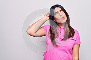 Young beautiful brunette woman wearing casual pink t-shirt standing over white background confuse and wondering about question