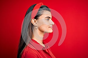 Young beautiful brunette woman wearing casual shirt and diadem over red background looking to side, relax profile pose with