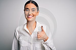 Young beautiful brunette woman wearing casual shirt over isolated white background doing happy thumbs up gesture with hand