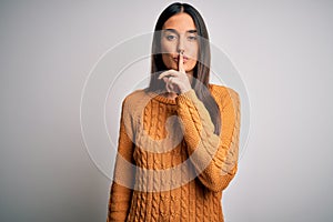 Young beautiful brunette woman wearing casual sweater over isolated white background asking to be quiet with finger on lips