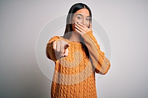 Young beautiful brunette woman wearing casual sweater over isolated white background laughing at you, pointing finger to the