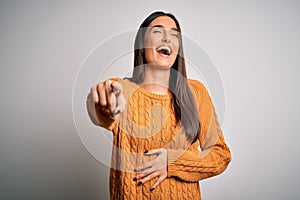 Young beautiful brunette woman wearing casual sweater over isolated white background laughing at you, pointing finger to the