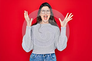 Young beautiful brunette woman wearing casual sweater over red background celebrating mad and crazy for success with arms raised