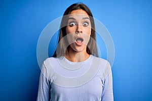 Young beautiful brunette woman wearing casual sweater standing over blue background afraid and shocked with surprise and amazed