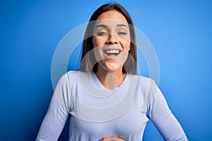 Young beautiful brunette woman wearing casual sweater standing over blue background smiling and laughing hard out loud because