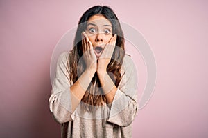 Young beautiful brunette woman wearing casual sweater standing over pink background afraid and shocked, surprise and amazed
