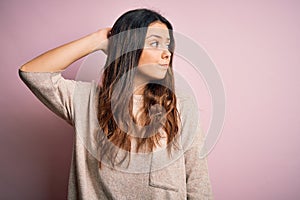Young beautiful brunette woman wearing casual sweater standing over pink background confuse and wondering about question