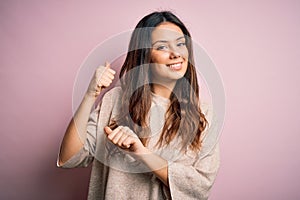 Young beautiful brunette woman wearing casual sweater standing over pink background Pointing to the back behind with hand and