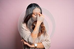 Young beautiful brunette woman wearing casual sweater standing over pink background tired rubbing nose and eyes feeling fatigue