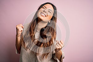 Young beautiful brunette woman wearing casual sweater standing over pink background very happy and excited doing winner gesture