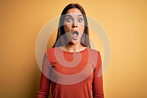 Young beautiful brunette woman wearing casual t-shirt standing over yellow background afraid and shocked with surprise and amazed