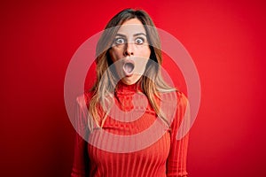 Young beautiful brunette woman wearing casual turtleneck sweater over red background afraid and shocked with surprise and amazed
