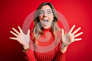 Young beautiful brunette woman wearing casual turtleneck sweater over red background celebrating crazy and amazed for success with