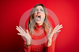 Young beautiful brunette woman wearing casual turtleneck sweater over red background celebrating mad and crazy for success with