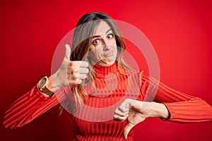Young beautiful brunette woman wearing casual turtleneck sweater over red background Doing thumbs up and down, disagreement and