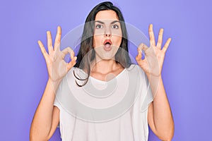 Young beautiful brunette woman wearing casual white t-shirt over purple background looking surprised and shocked doing ok approval